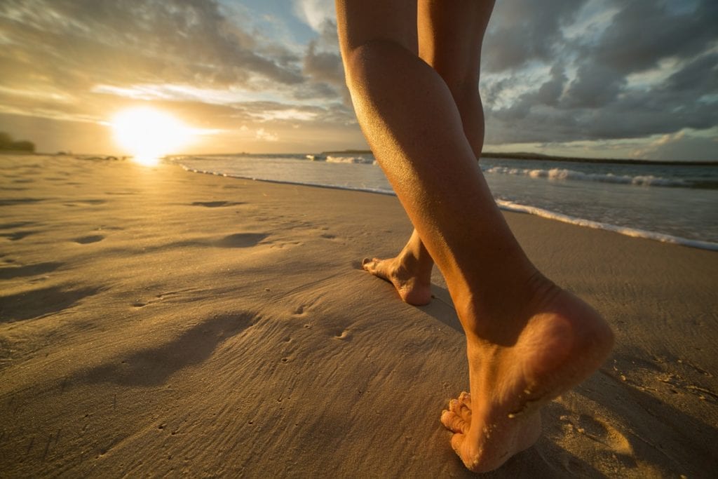 barefoot-on-beach-walking-towards-sunlight-waxmd